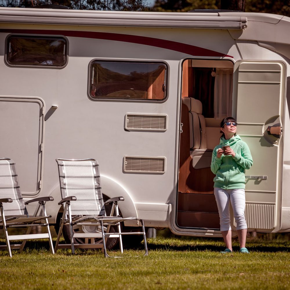 Woman is standing with a mug of coffee near the camper. Caravan car Vacation. Family vacation travel, holiday trip in motorhome RV