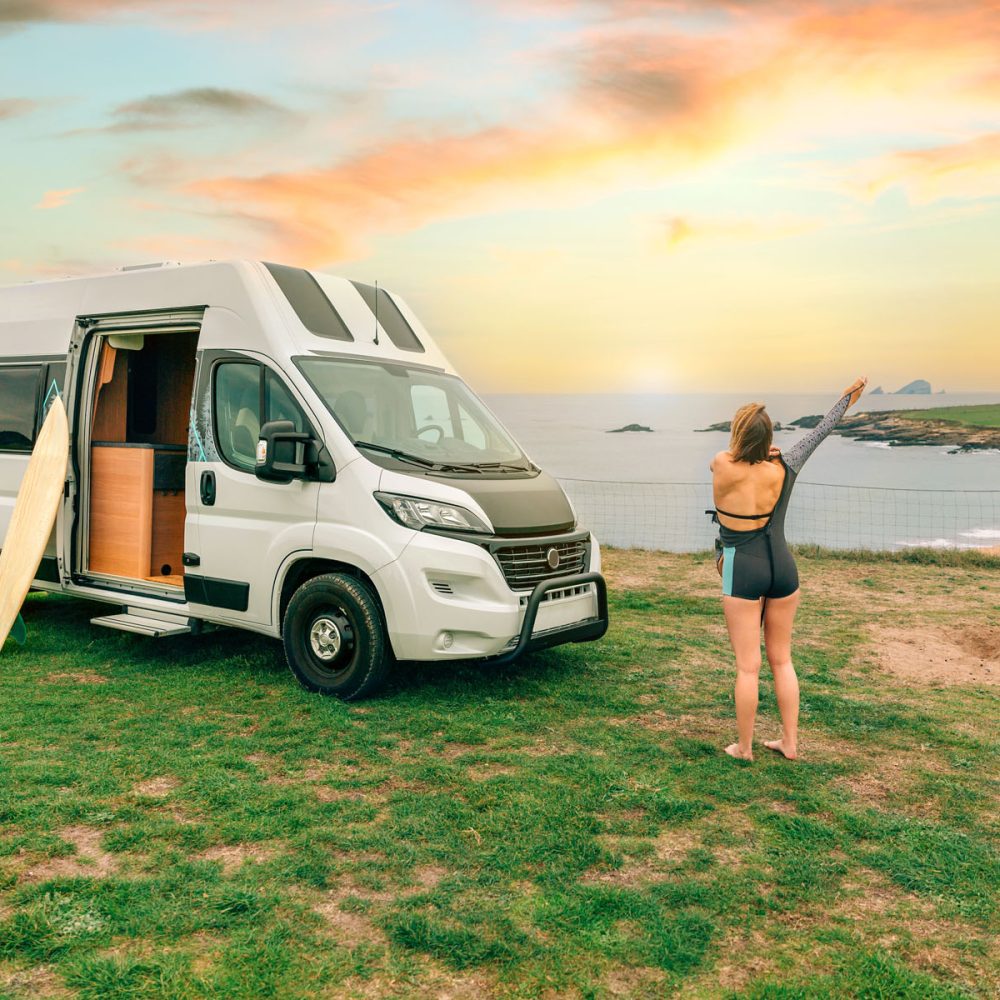 Unrecognizable young woman putting on her wetsuit for surfing next to her camper van